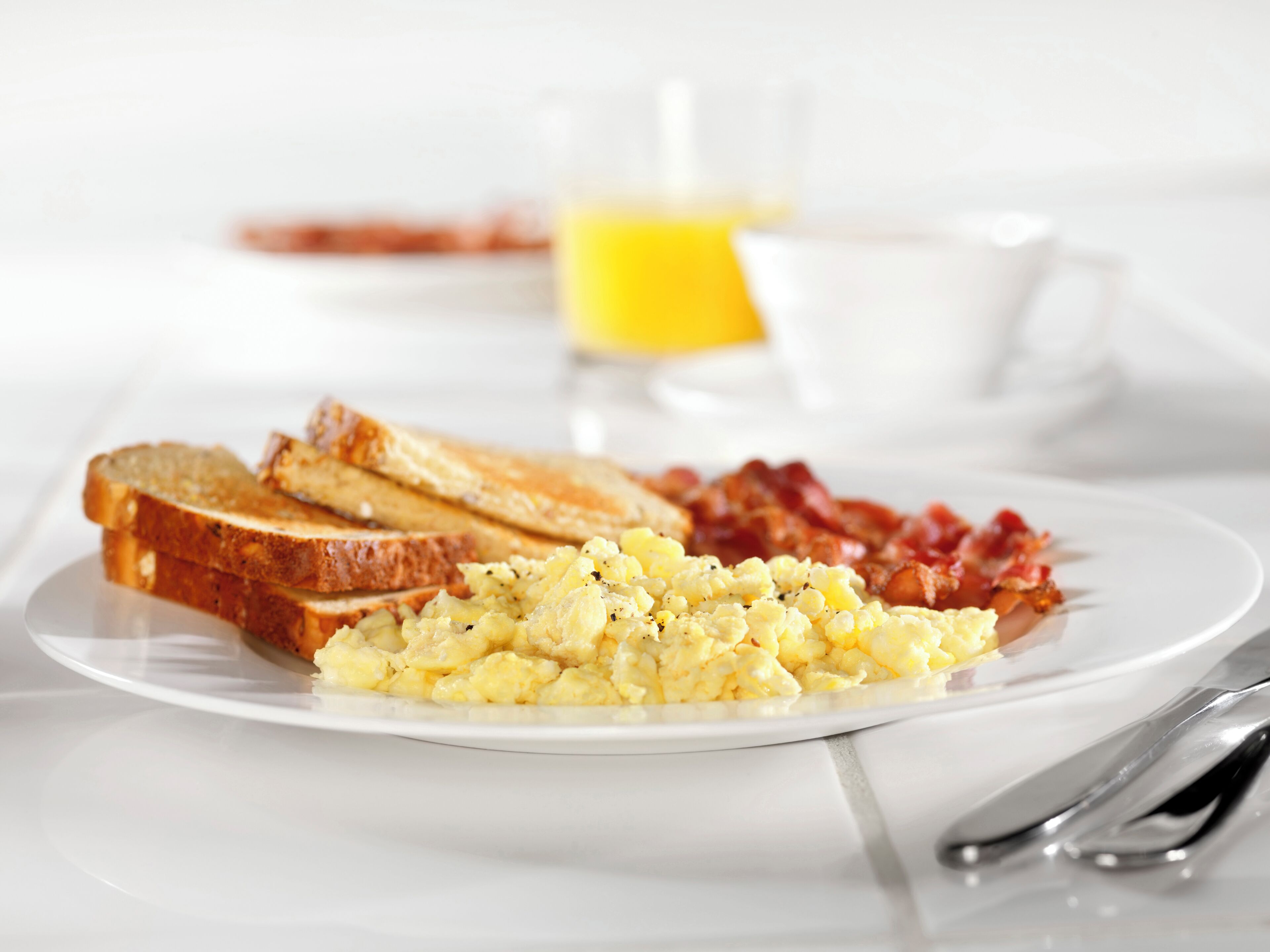 A breakfast plate with scrambled eggs, bacon, and toast on a white plate.