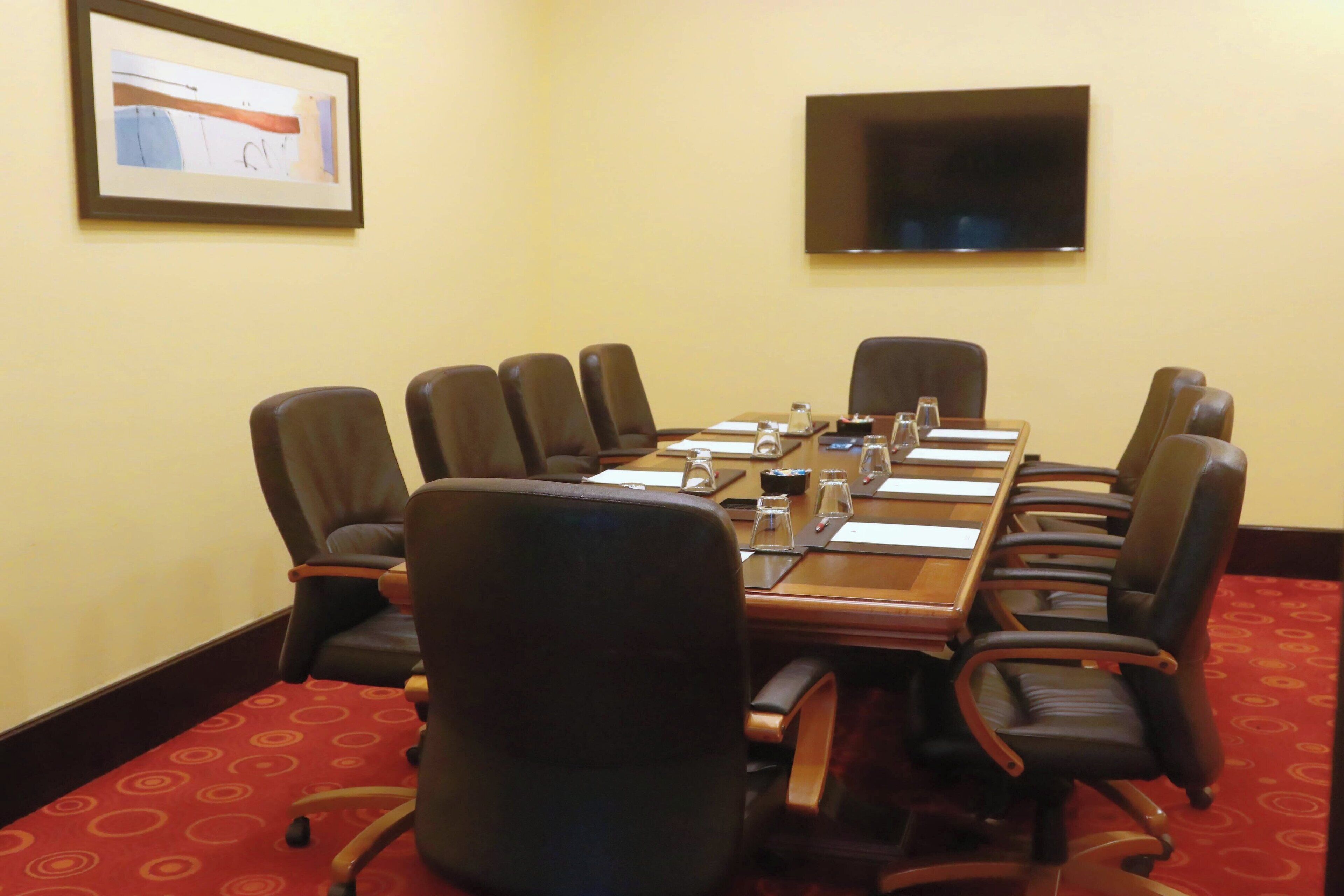 Un salón de conferencias con una larga mesa, múltiples sillas, un televisor de pantalla plana y un cuadro en la pared.
