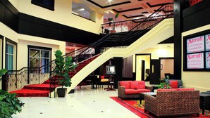 Eine Hotellobby mit Treppe, rotem Teppich, Korbmöbeln und einem großen Bildschirm mit dem Marriott-Logo.