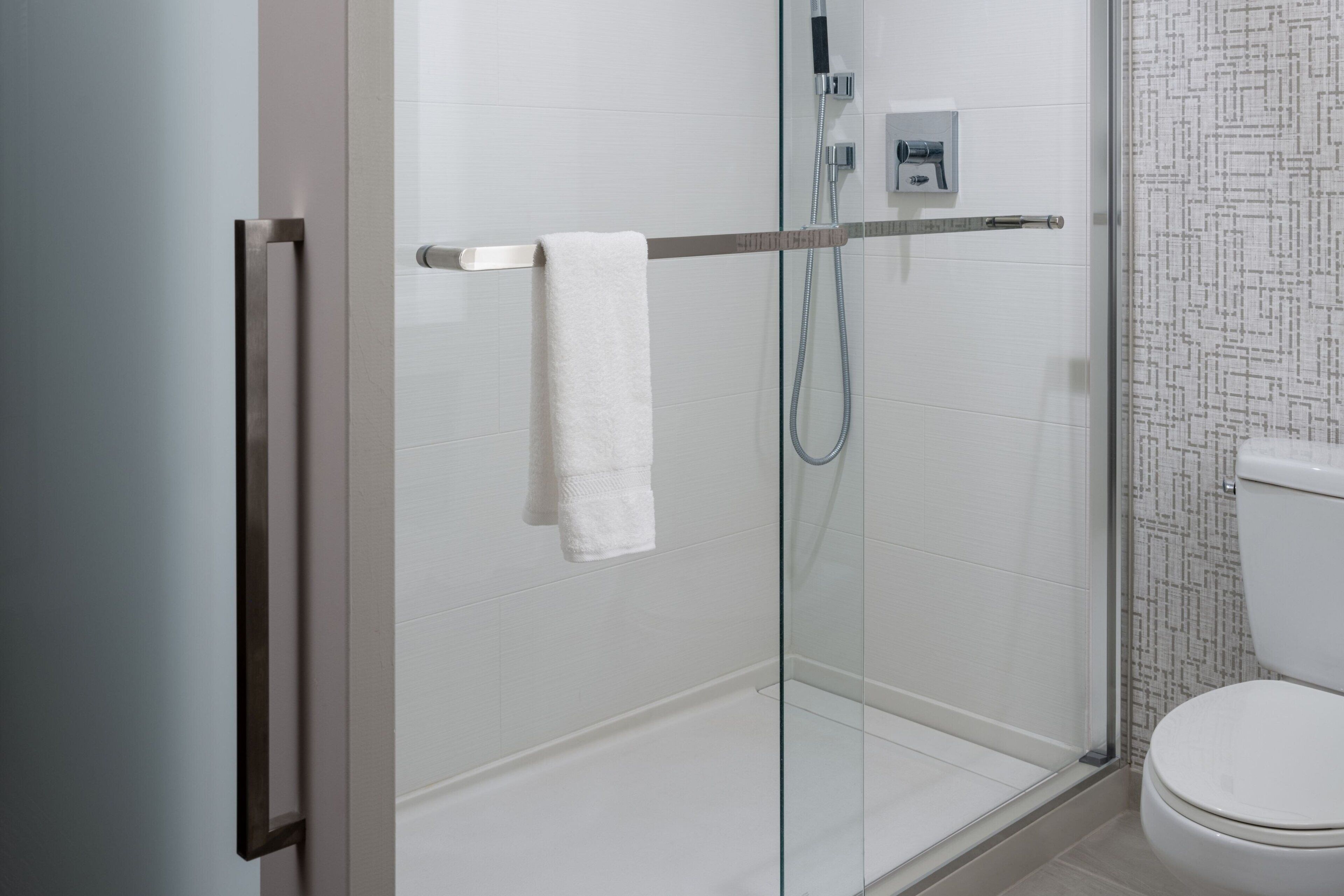 A modern bathroom with a glass shower enclosure, a white toilet, and a towel rack.