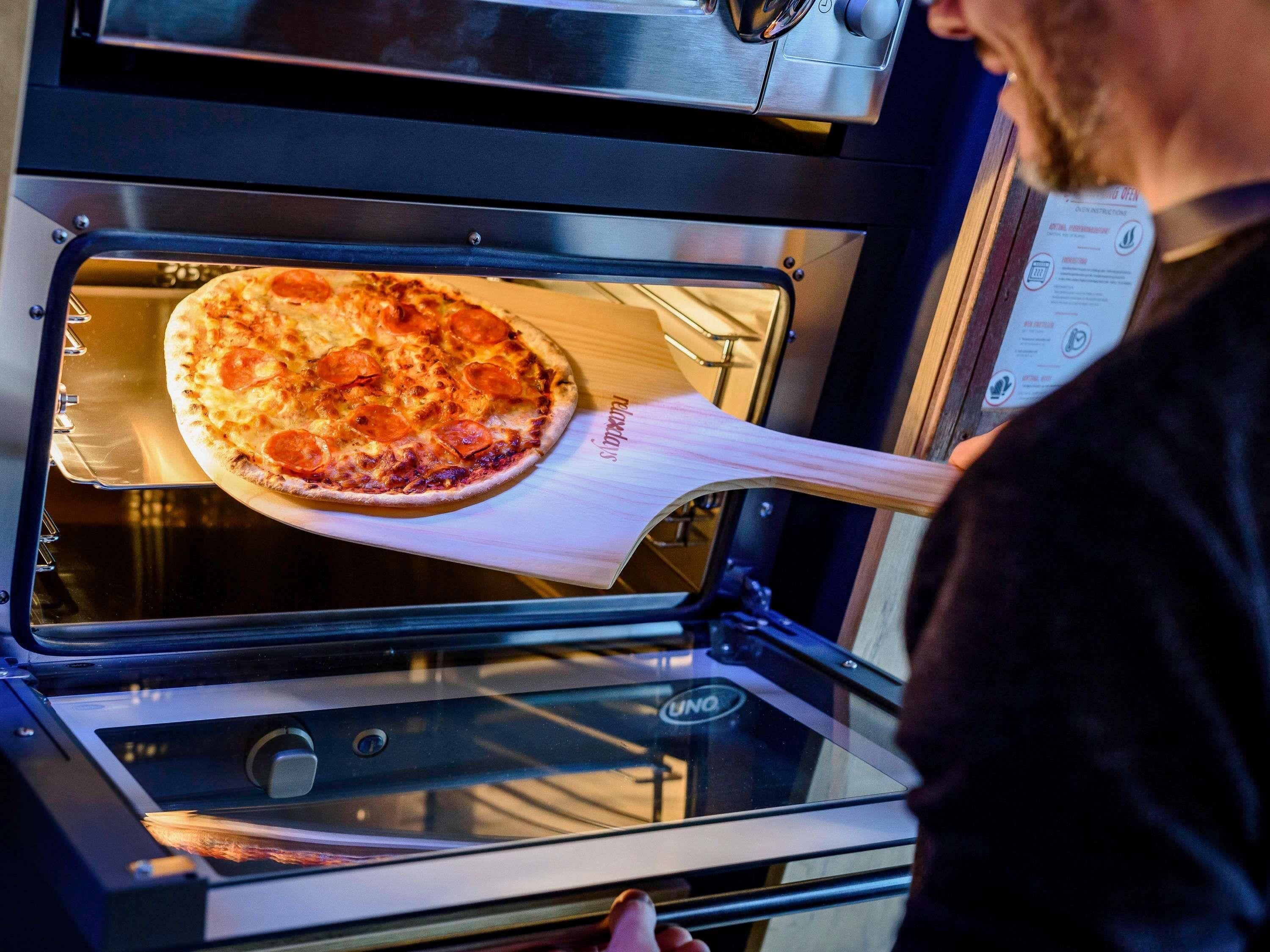 Una pizza siendo sacada de un horno con una pala de madera.