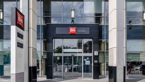 La entrada del hotel ibis Berlin Spandau, con fachada de vidrio moderna y un panel digital que muestra la disponibilidad de habitaciones.
