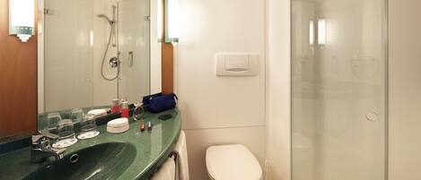 A bathroom with a green sink, a white toilet, a glass shower enclosure, and a mirror with lights.