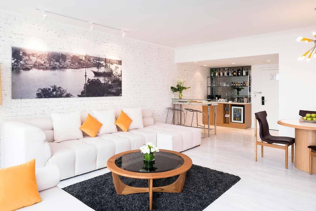 A modern living room with a white sofa, a round coffee table, and a kitchen area with a bar.