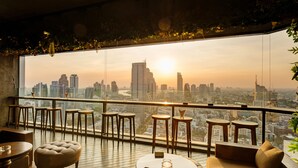 A high-rise room with a city view, wooden flooring, and modern furniture including a sofa, ottoman, and round tables. - Pullman Bangkok Hotel G (Bangkok)