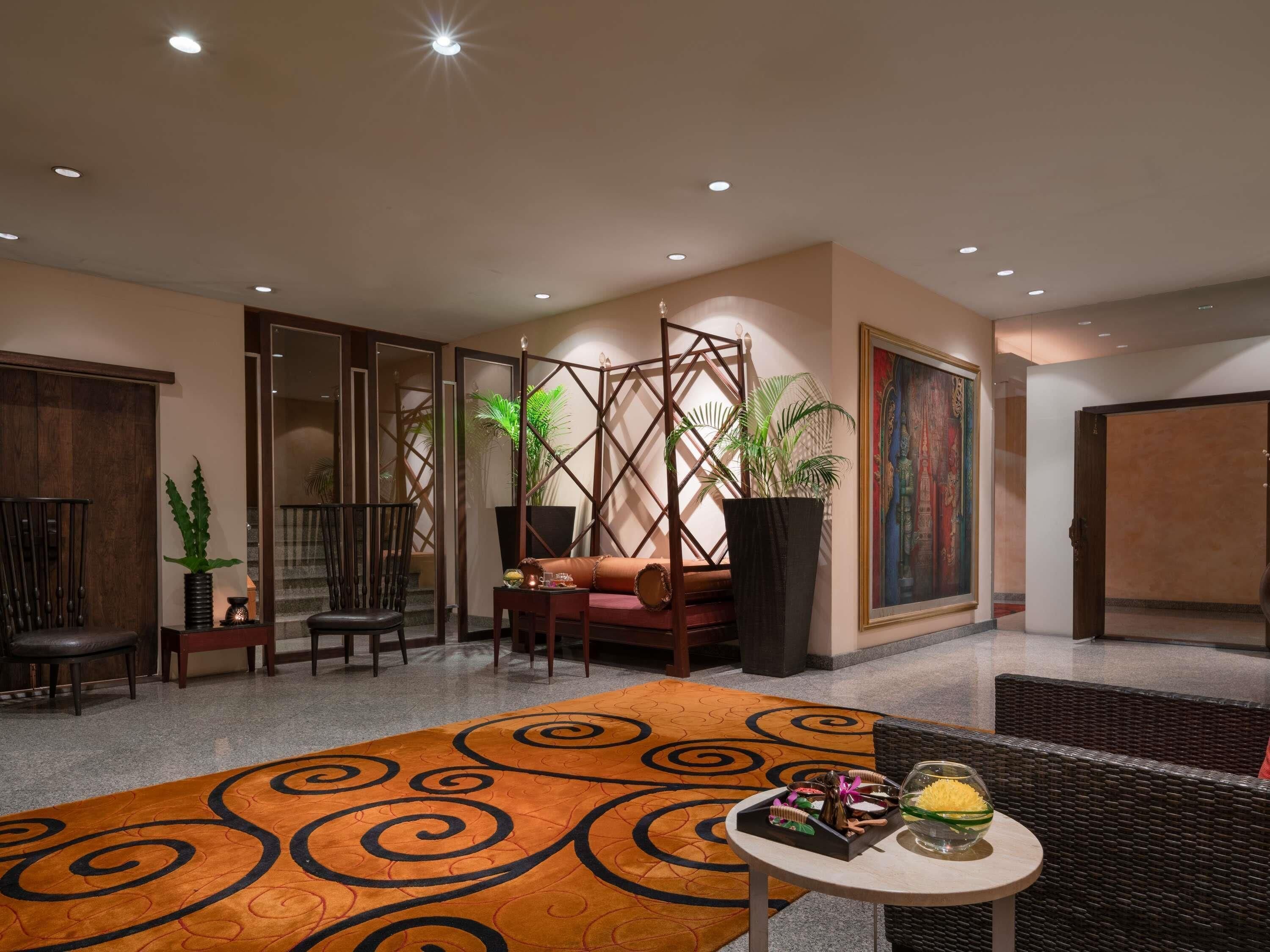 Un hall d’entrée avec un tapis à motifs, un espace salon, des plantes en pot et un tableau accroché au mur.