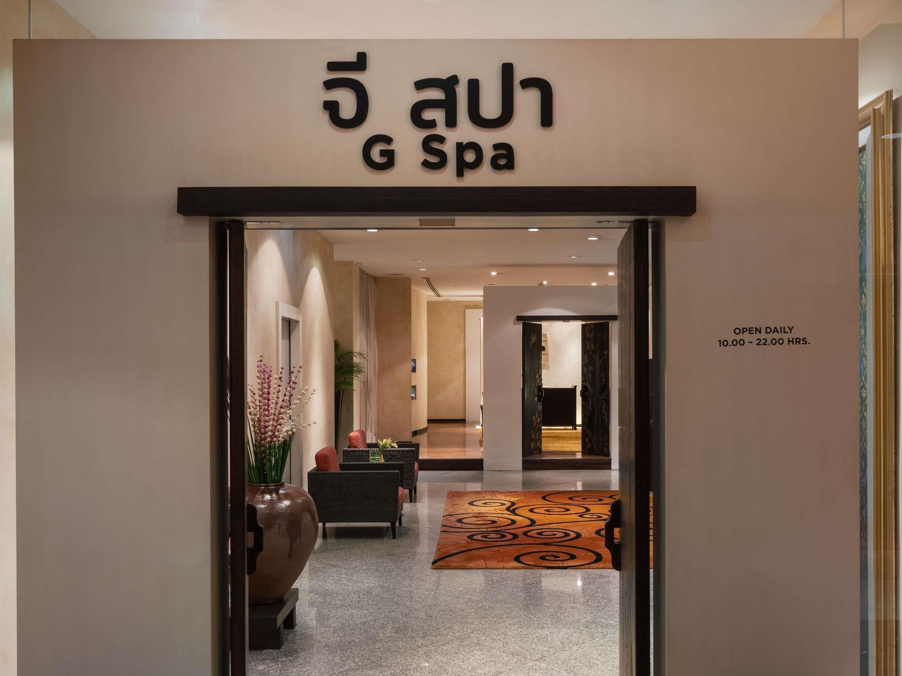 Entree van een spa, met een bordje dat 'G Spa' vermeldt en een glazen deur. Binnen is een receptie met een balie, een potplant en een decoratief vloerkleed.