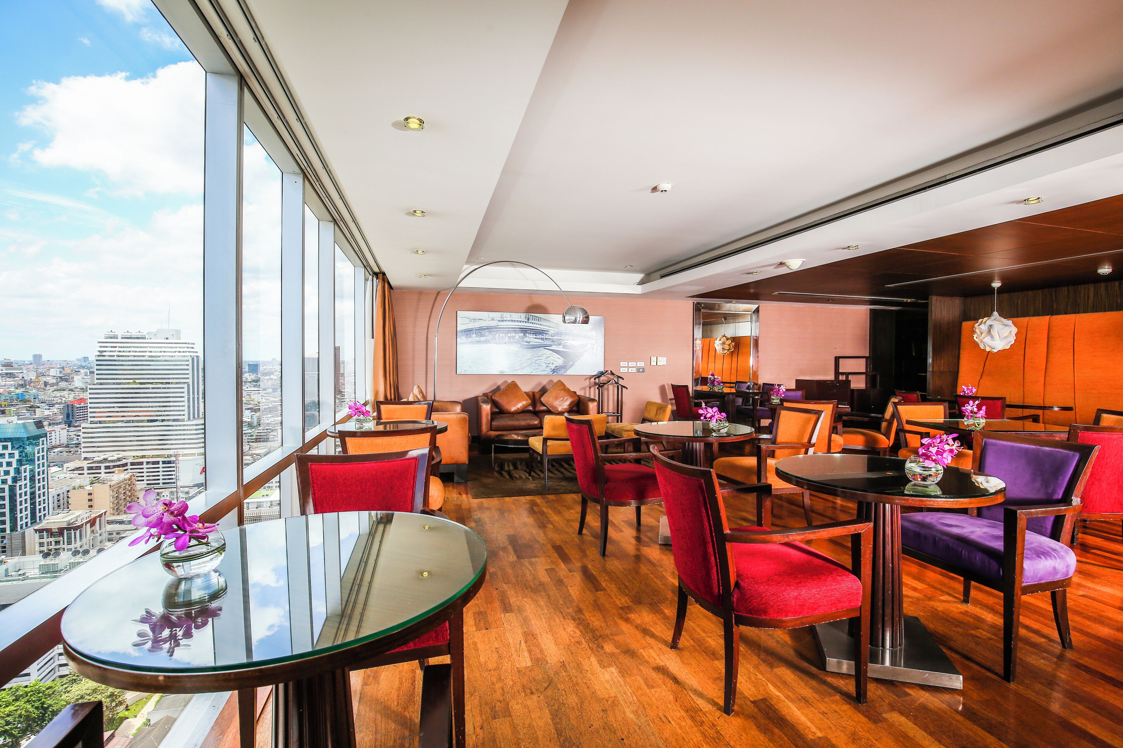 Un hall d’hôtel moderne avec vue sur la ville, un grand écran et différents espaces aménagés pour s’asseoir.
