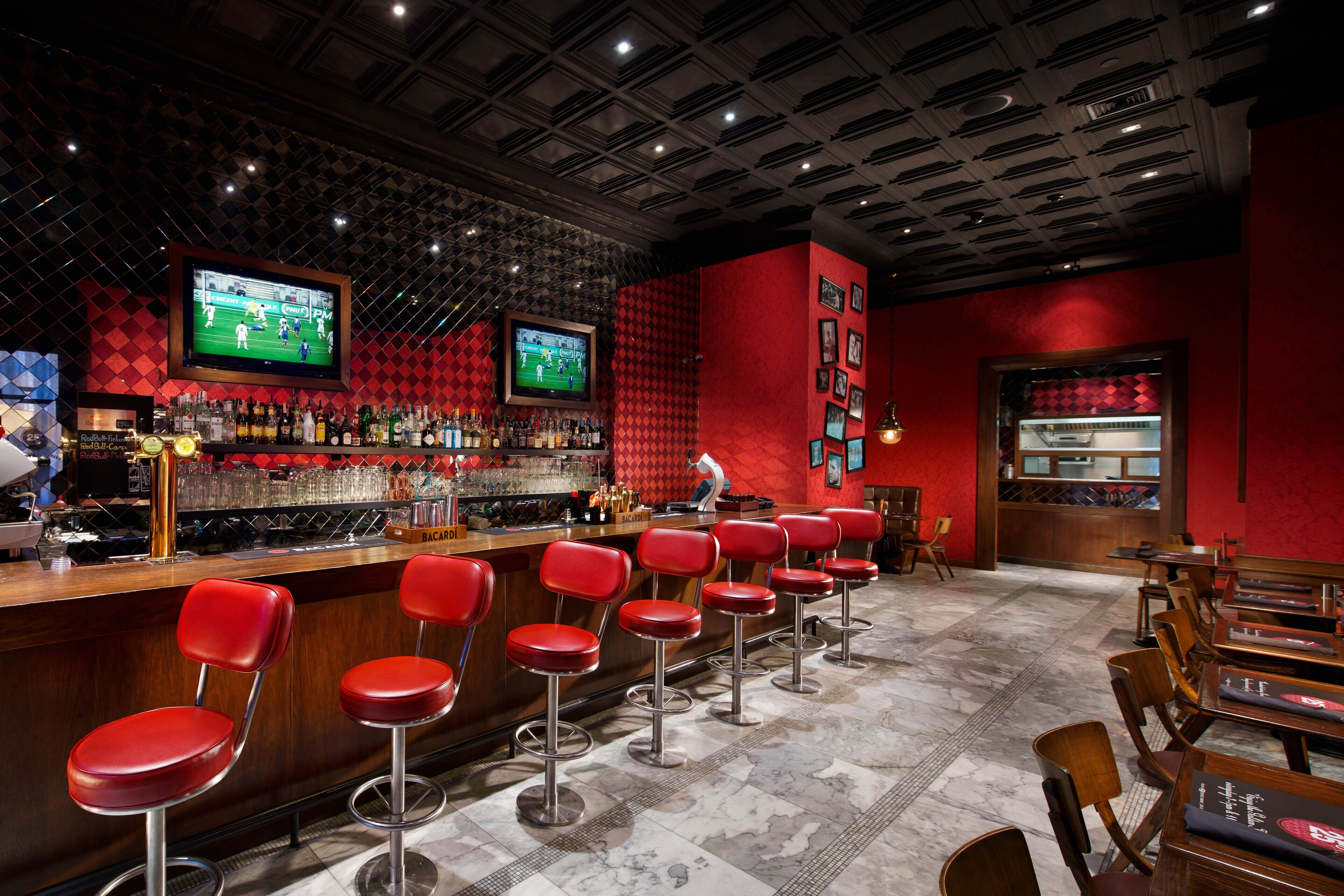 Zona de bar con taburetes rojos, una barra con pantalla de televisión y una pared roja decorada con cuadros.