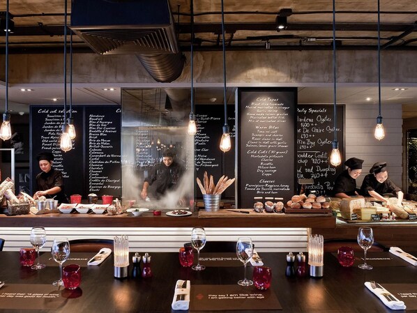 A restaurant interior with a menu board, chef preparing food, and wine glasses on the table. - Pullman Bangkok Hotel G (Bangkok)