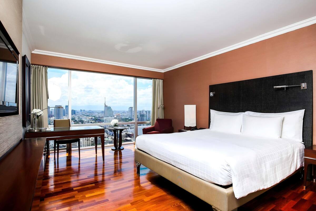 A hotel room with a large bed, a desk, a chair, and a view of the cityscape.