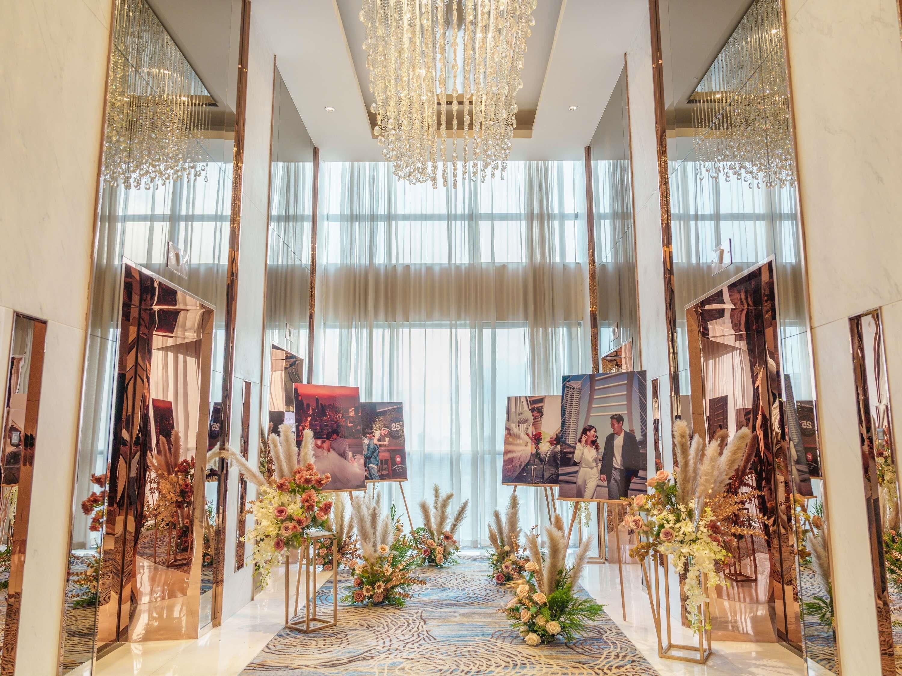 A grand hallway with a chandelier, large windows, and framed photos on stands.