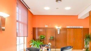 A modern waiting area with orange walls, a round table with chairs, and a sign reading "SALÓN LA ENCINA". - Hotel Ponferrada Plaza (Ponferrada)