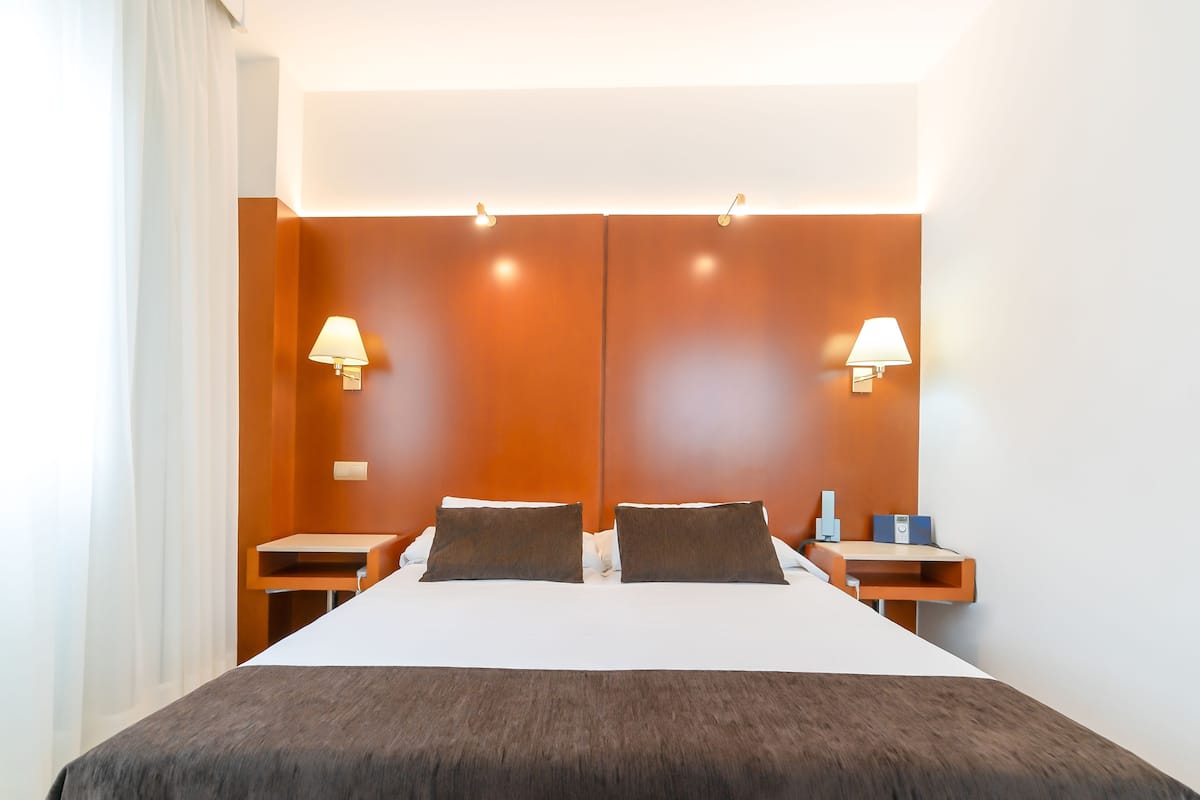 Una habitación de hotel moderna con una cama grande, dos mesitas de noche y lámparas fijadas a la pared.