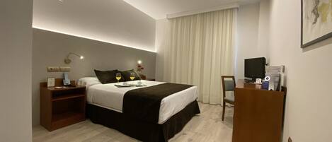 Una habitación de hotel moderna con una cama grande, mesitas de noche, un escritorio con una computadora y un televisor.
