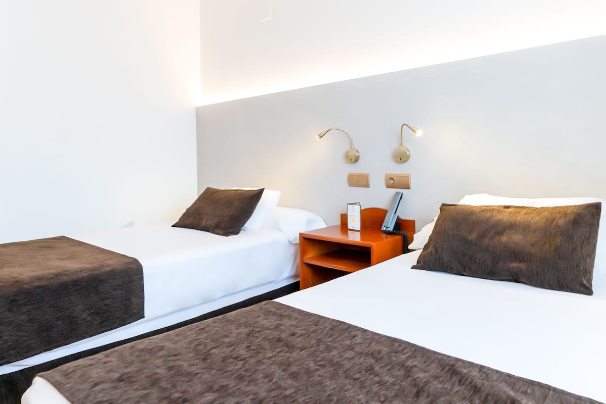 Habitación de hotel con dos camas, una mesita de noche, una lámpara y una luz empotrada en la pared.