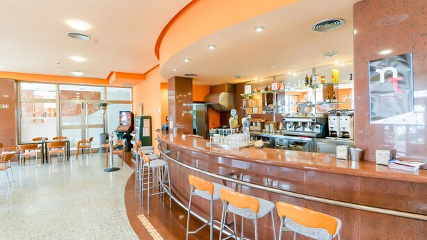 A modern bar area with a curved counter, multiple stools, and a seating area with tables and chairs. - Hotel Ponferrada Plaza (Ponferrada)