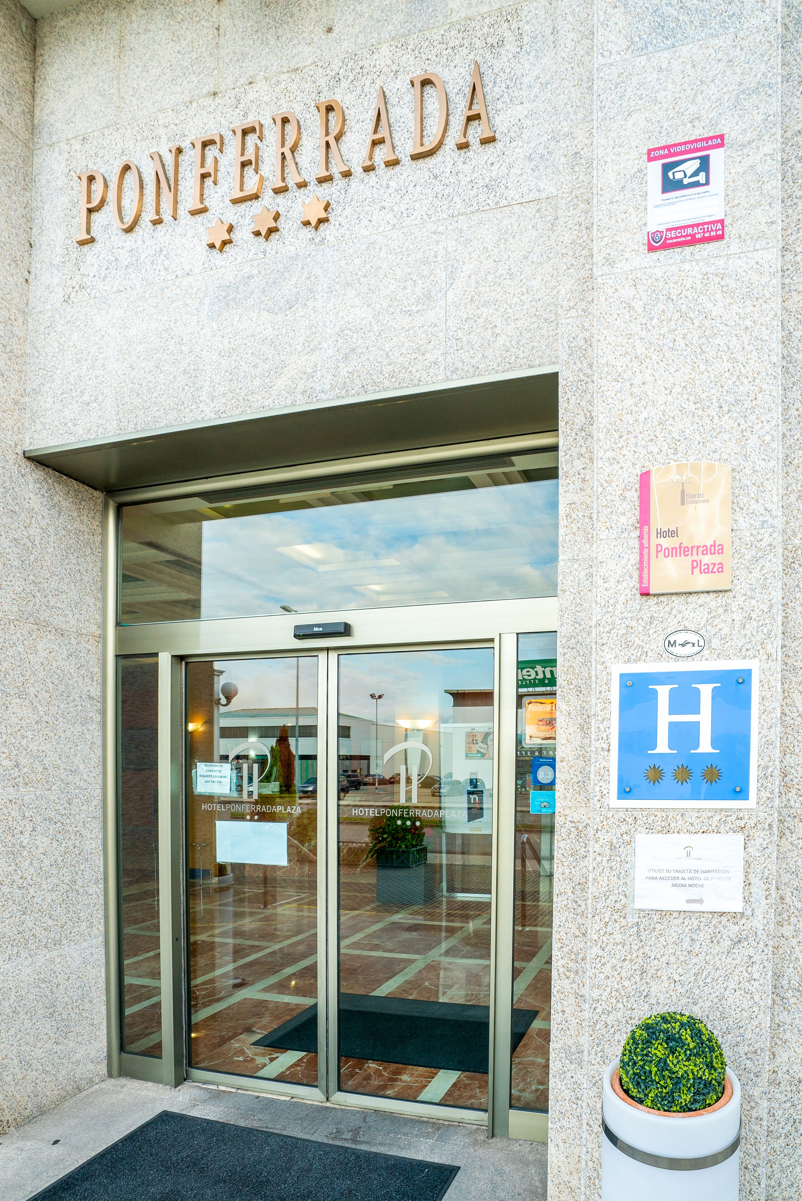 L’entrée de l’hôtel Ponferrada Plaza se distingue par une porte en verre, une enseigne indiquant le nom de l’hôtel et un pot de fleurs placé sur le côté droit.