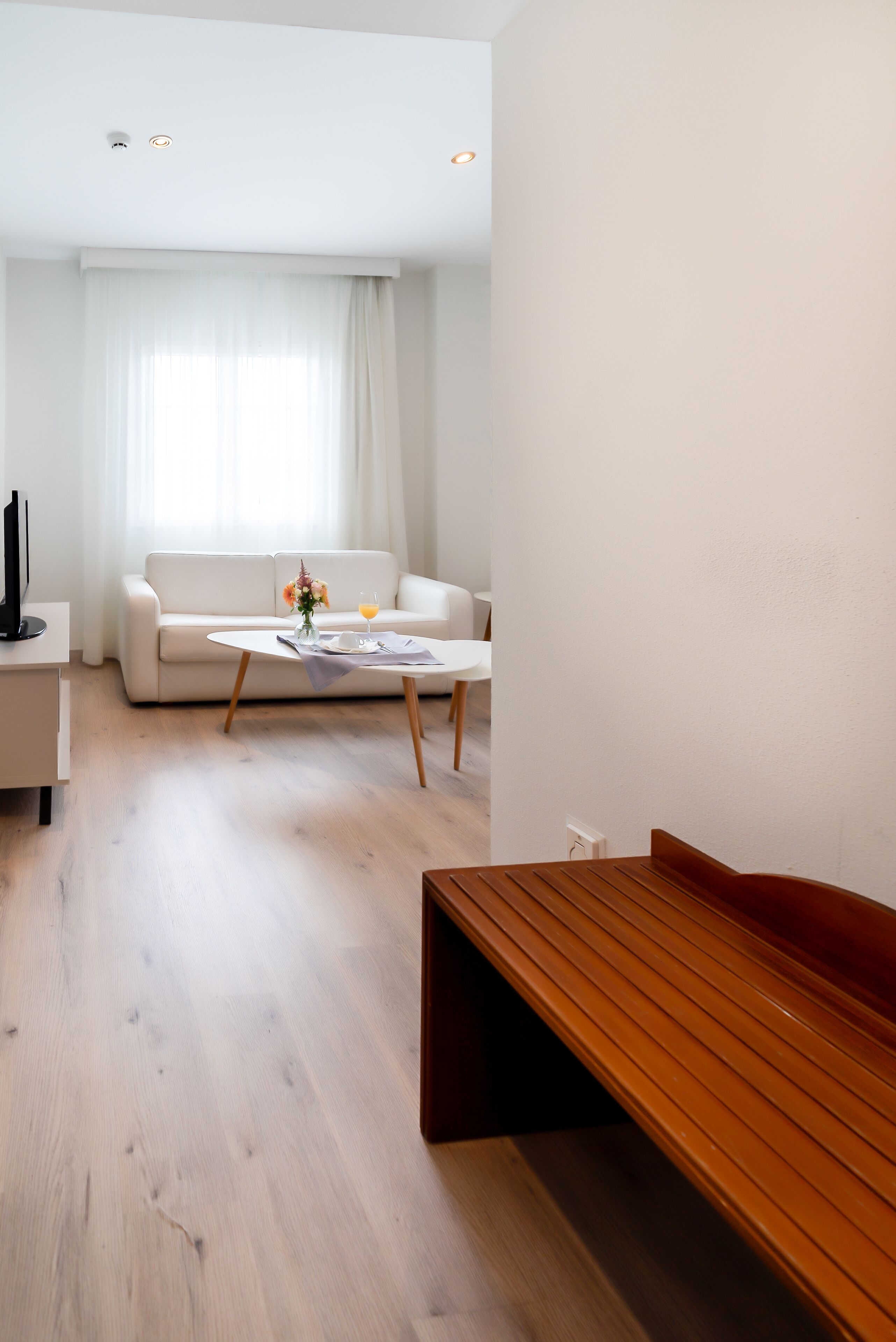 A modern living room with a white sofa, a coffee table, and a wooden bench.