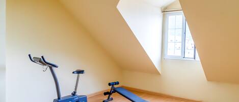 Una habitación con piso de madera, una bicicleta apoyada, un banco y un tragaluz.