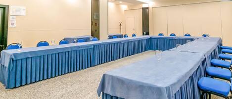 Un salón de conferencias con una larga mesa, sillas azules y piso alfombrado.