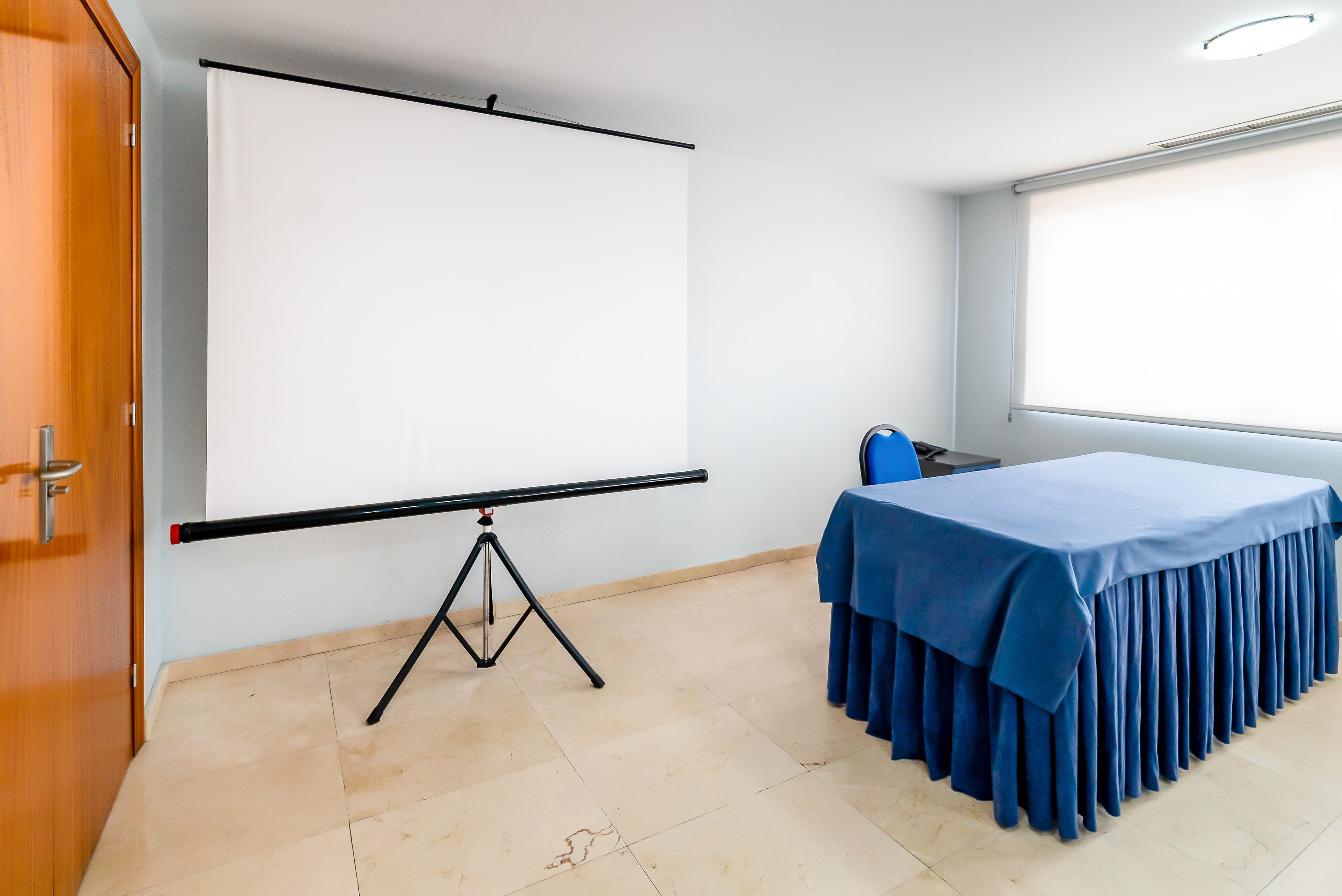A conference room with a projection screen, a table with a blue tablecloth, and a window.