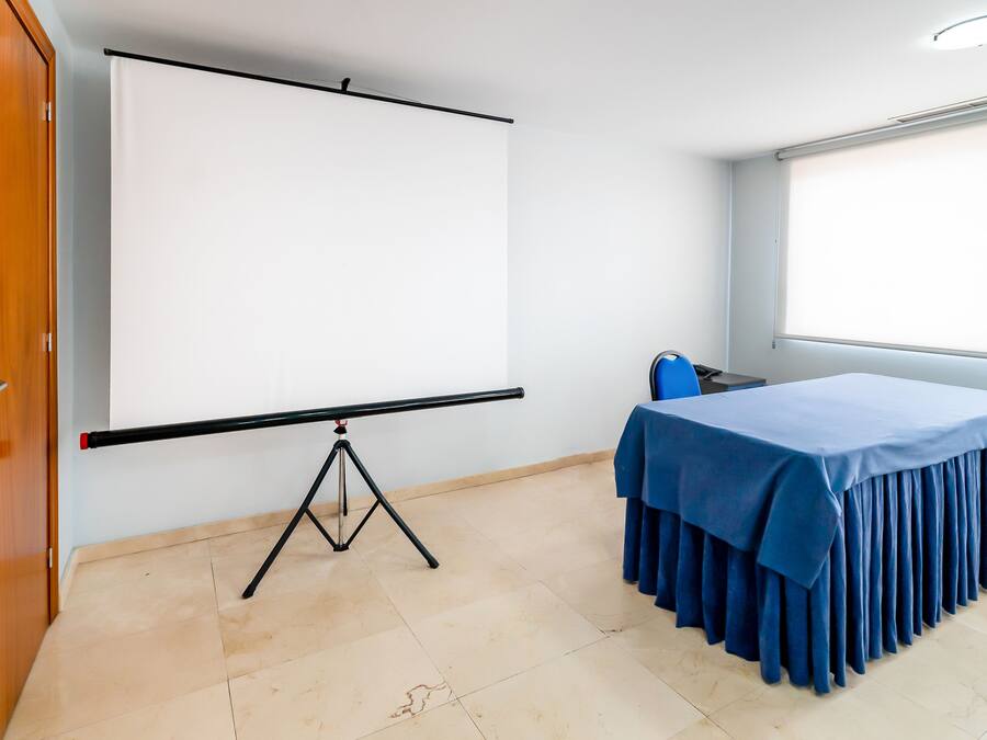 A conference room with a projection screen, a table with a blue tablecloth, and a window.