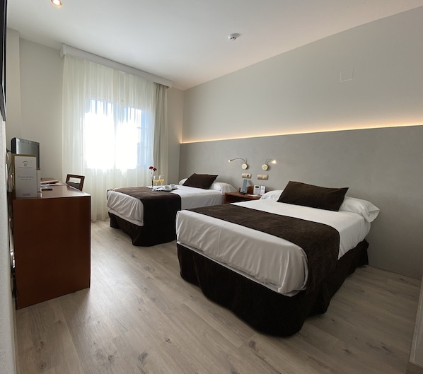 Habitación de hotel con dos camas, un escritorio y una ventana con cortinas.