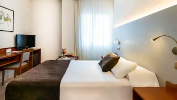 Habitación de hotel con cama, escritorio con computadora, silla, televisor y ventana con cortinas.