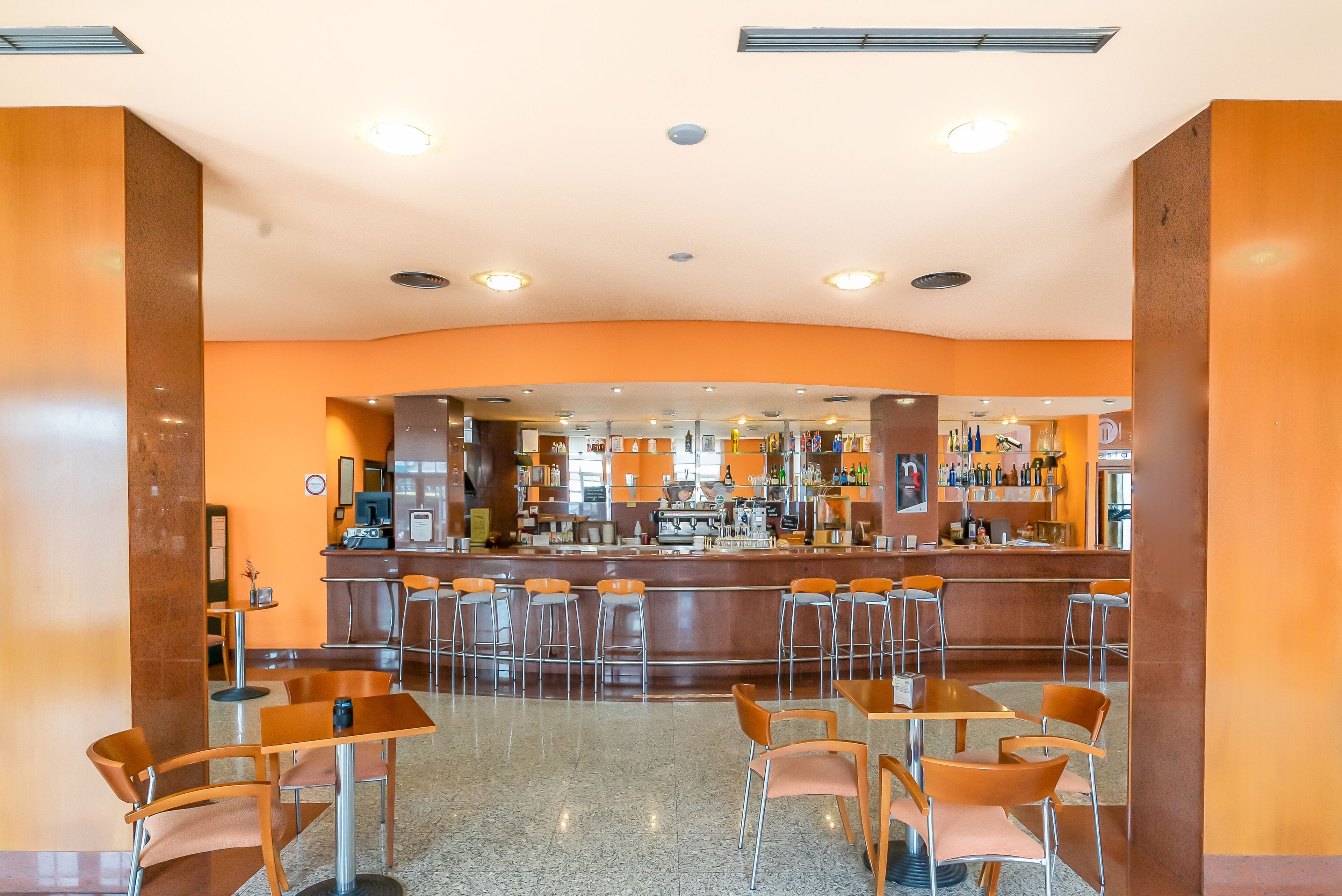 Zona de bar moderna con una barra curva, varios taburetes y una máquina de café.
