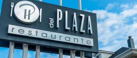 Un letrero que dice 'Plaza Restaurante' con tres banderas en palos.