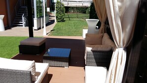 An outdoor patio area with a sofa, a small table, and a wicker chair. There is a staircase leading to an upper level, and a well-maintained lawn in the background. - Hotel Ponferrada Plaza (Ponferrada)