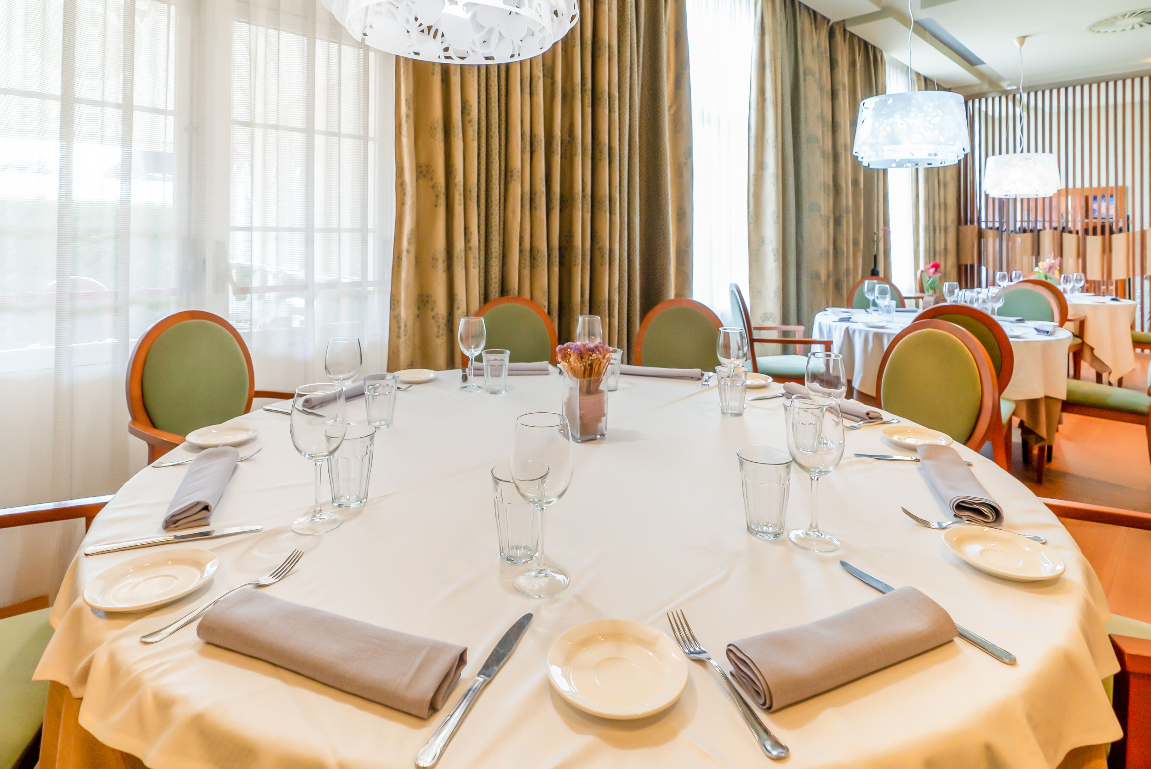 A round dining table set with plates, cutlery, and glasses, surrounded by chairs.