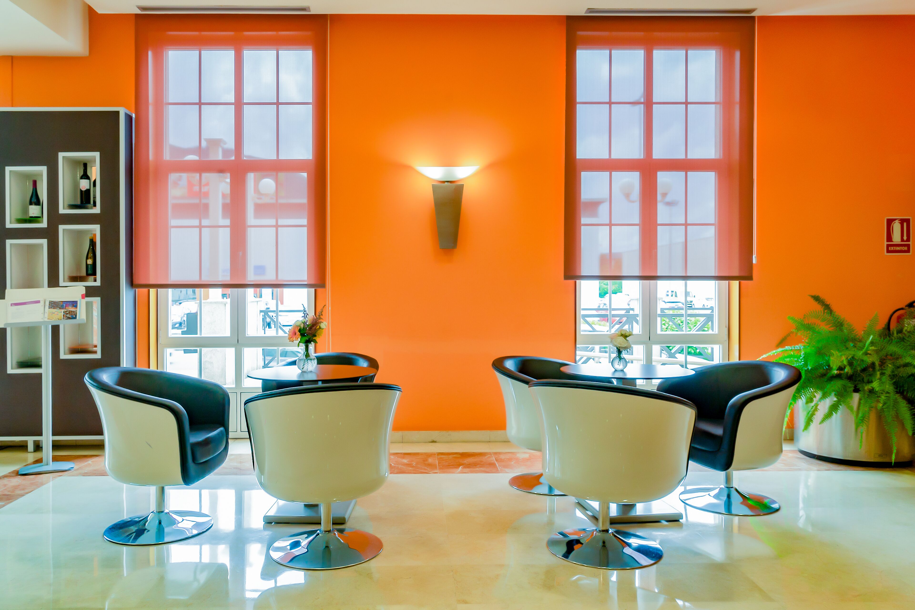 A modern room with orange walls, a large window, and three white chairs with black seats.