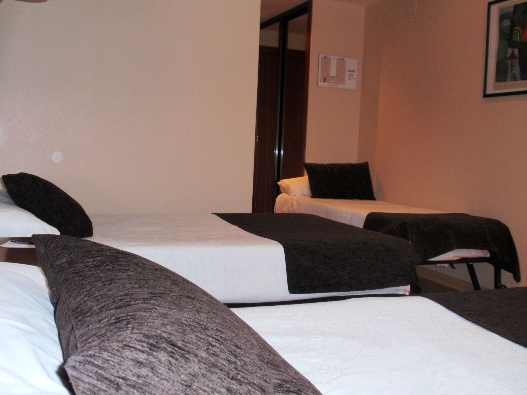 A room with three beds arranged in a row, each with a black headboard and white bedding.