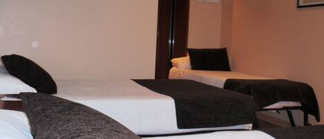 A room with three beds arranged in a row, each with a black headboard and white bedding.