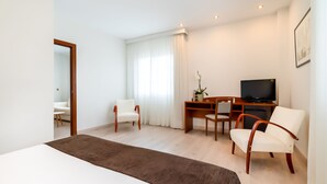 A hotel room with a large bed, a desk with a TV, two chairs, and a window with curtains. - Hotel Ponferrada Plaza (Ponferrada)