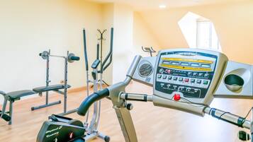 Ein Fitnessraum mit Trainingsgeräten, darunter Laufband und Kraftgeräte, mit Holzboden und einem großen Fenster.
