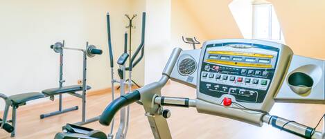 A gym with exercise equipment, including a treadmill and weight machines, in a room with wooden flooring and a large window.