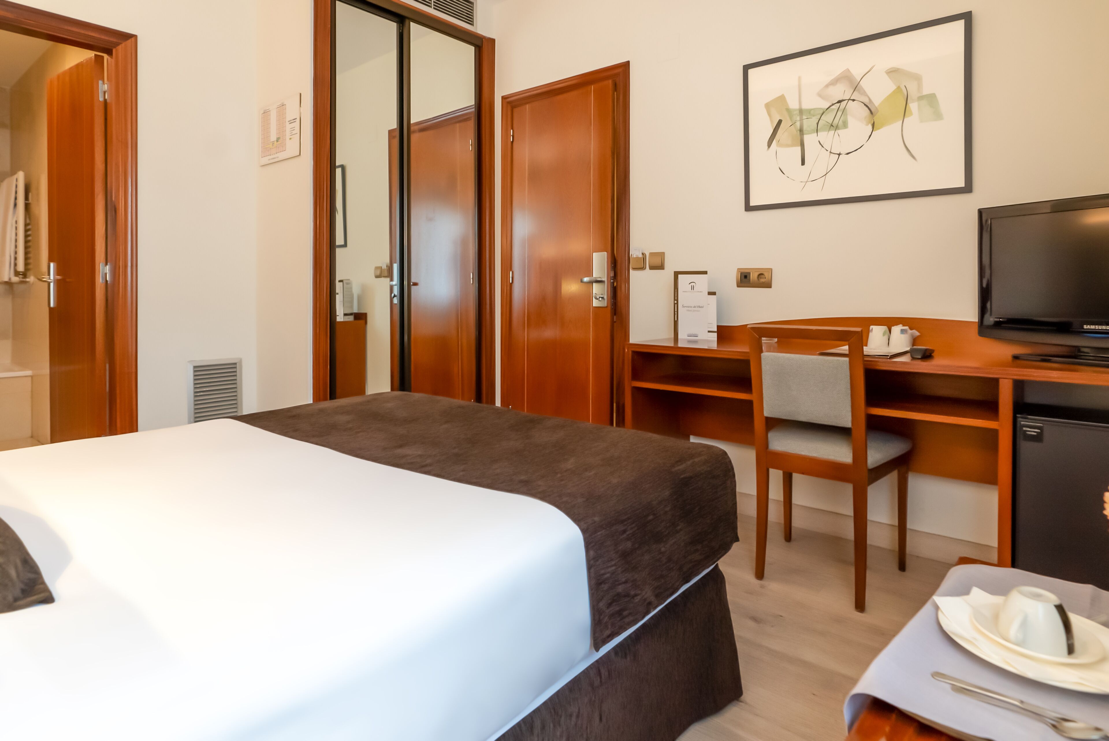 Una habitación de hotel con una cama, un escritorio con silla, un televisor y un refrigerador pequeño.