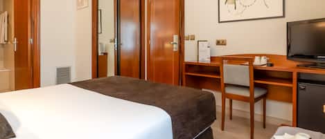 A hotel room with a bed, a desk with a chair, a television, and a small refrigerator.