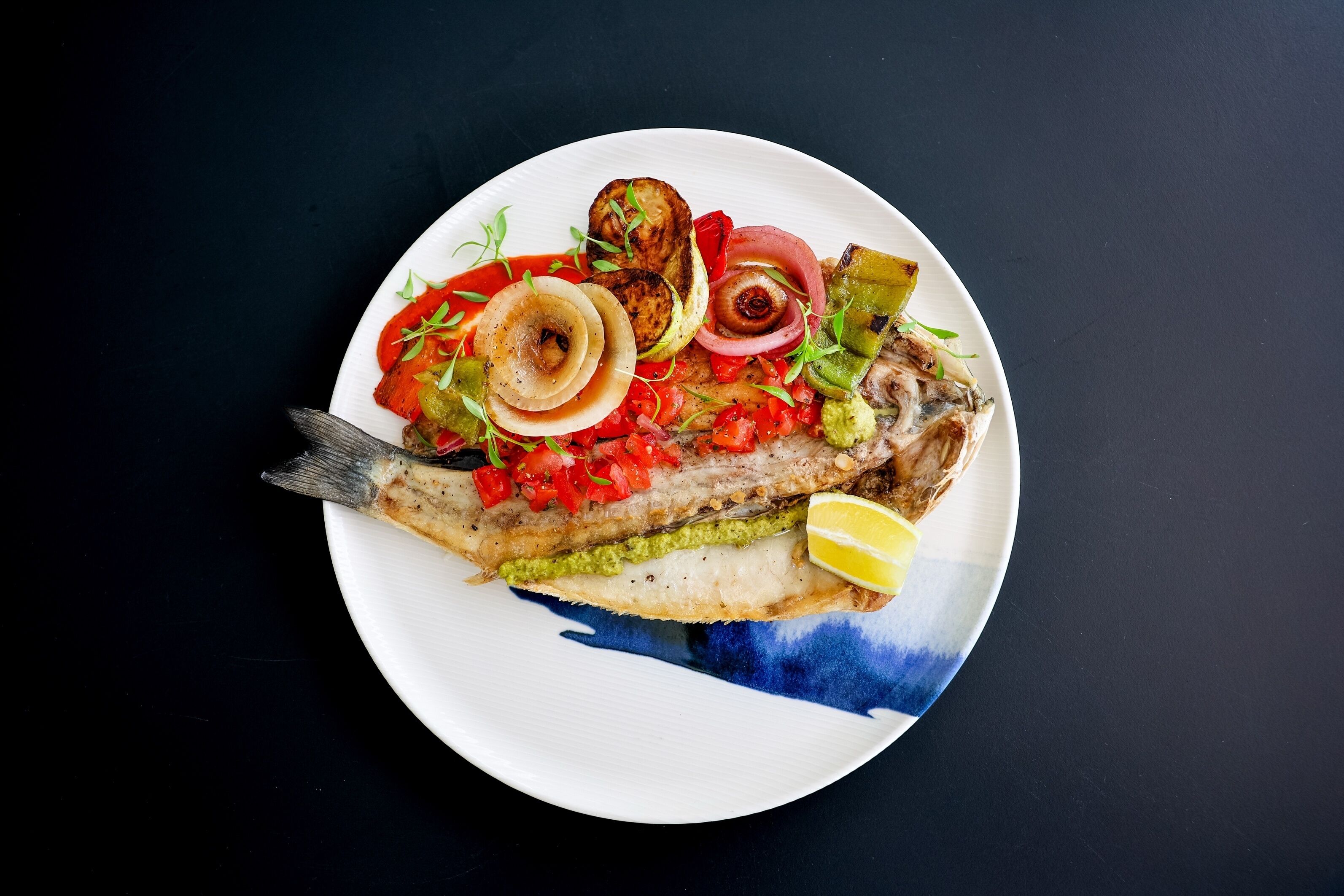 A plate of grilled fish with vegetables and a lemon wedge.