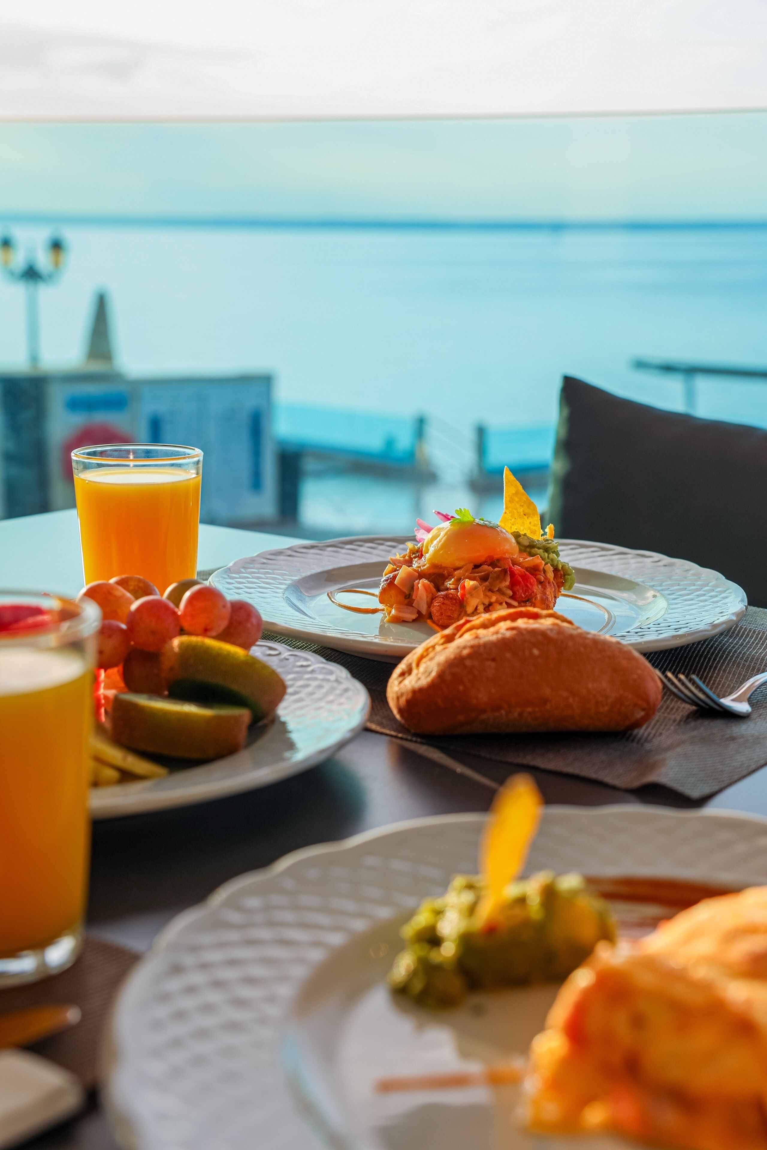 A table with breakfast items including a glass of orange juice, a plate with a sandwich, and a plate with fruit and a small dish.