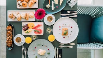 Morgenmad med croissanter, kager, frugt og drikkevarer på et bord.