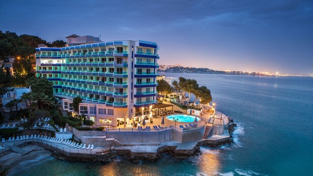 Un hotel de varios pisos con zona de piscina y vista al mar.