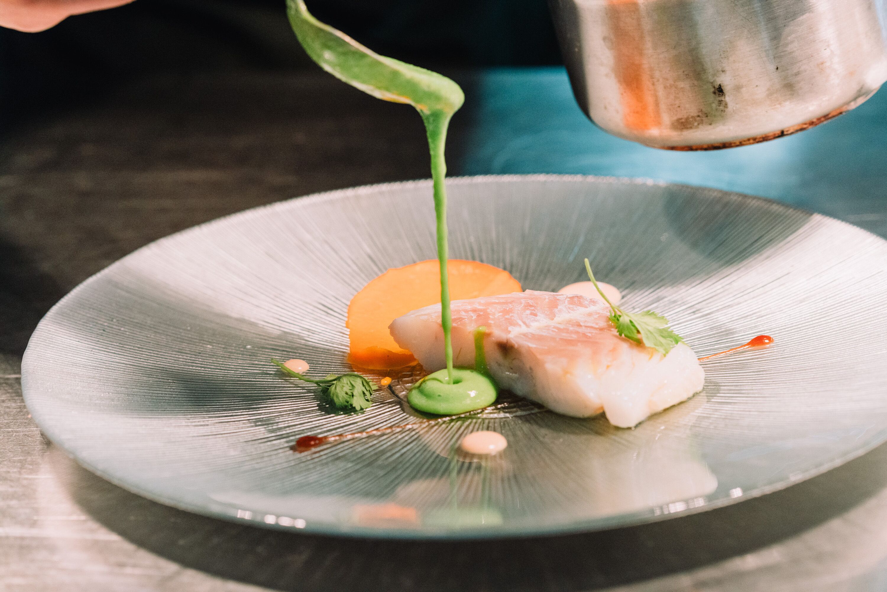 Ein Teller mit Fisch, Soße und Garnitur.