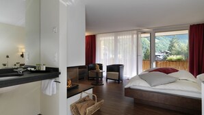A modern hotel room with a bed, a small seating area, a bathroom with a sink, and a view of the outdoors. - Hotel Schweizerhof Gourmet & Spa (Saas-Fee)