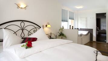 Una cama bien hecha con sábanas blancas y una rosa roja, un aplique en la pared y una ventana con persianas.