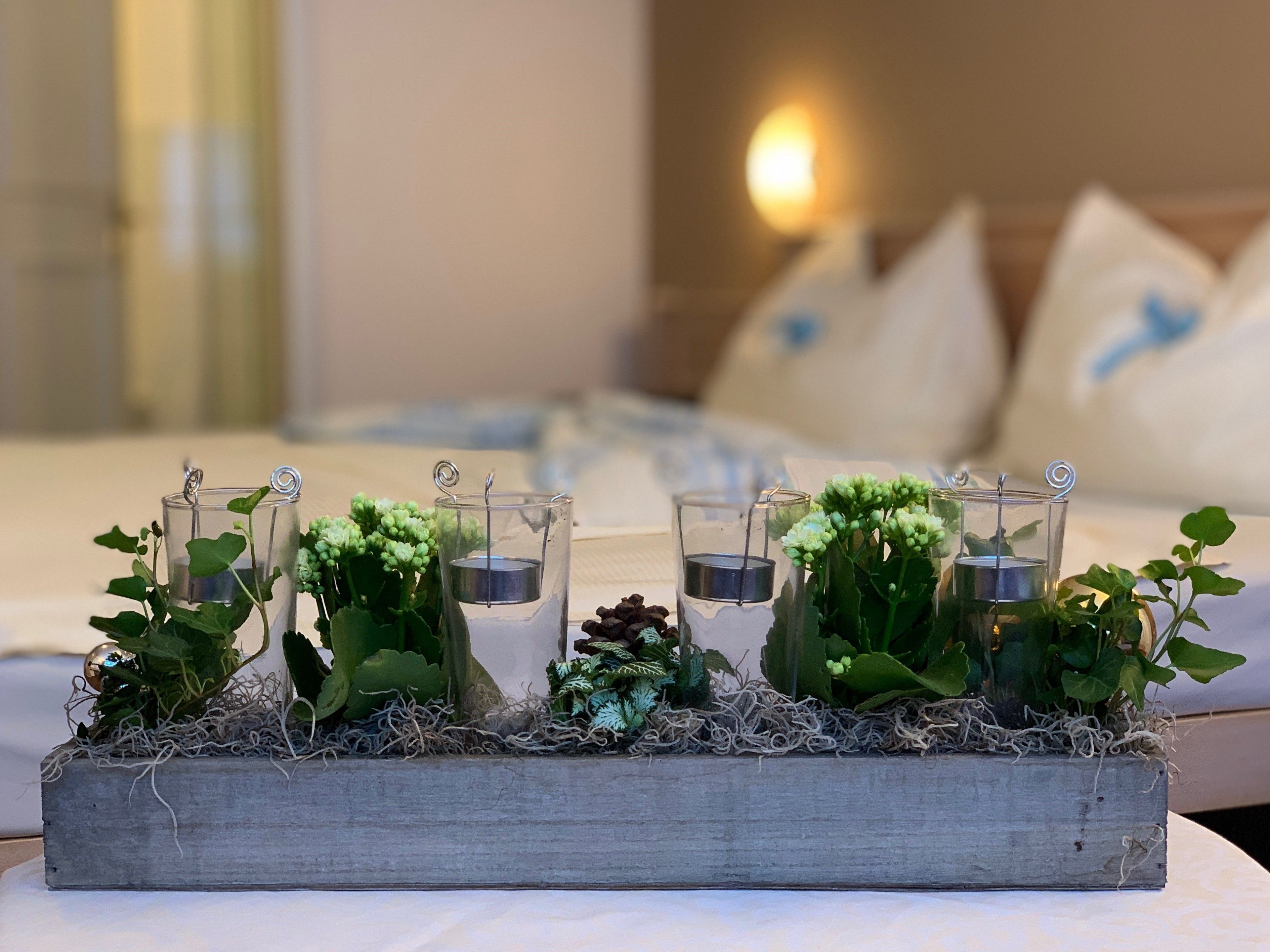 Una cama con cabecera de madera, almohadas y una mesita de noche con una decoración de candelabros de vidrio y plantas verdes.