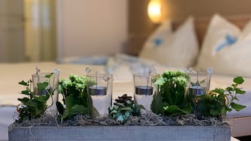 Una cama con cabecera de madera, almohadas y una mesita de noche con una decoración de candelabros de vidrio y plantas verdes.